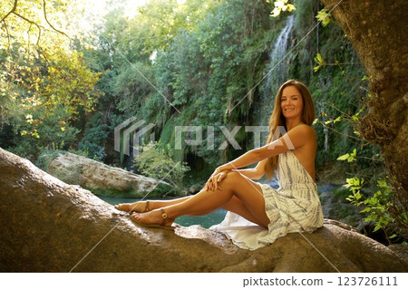 Smiling Woman Sitting on Tree Trunk Near Waterfall Smiling Woman Sitting on Tree Trunk Near Waterfall 123726111