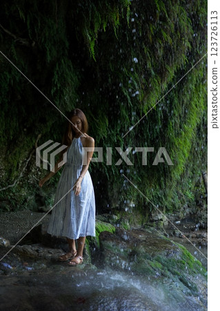 Woman Standing Peacefully Under a Gentle Waterfall Mist  123726113