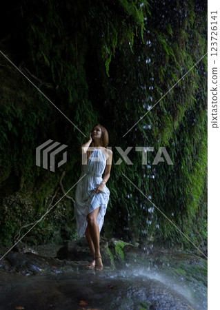Woman Enjoying the Mist of a Cascading Waterfall  123726141