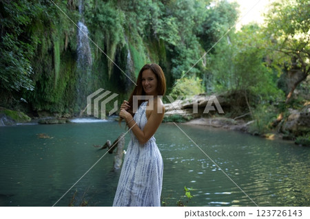 Smiling Woman Standing by a Scenic Waterfall and River  123726143