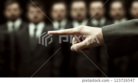 A hand points at several blurred figures dressed in suits. Concept of choice and decision-making. A hand points at several blurred figures dressed in suits. Concept of choice and decision-making. 123726547