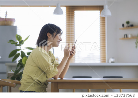 A woman in her 30s operating her smartphone at a table at home A woman in her 30s operating her smartphone at a table at home 123727568