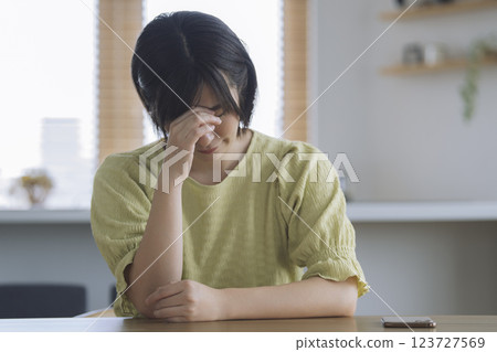 一位 30 多歲的女性在家中的餐桌旁抱著頭 123727569