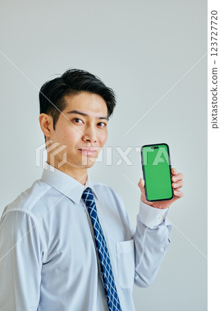 Young man in his 20s holding a smartphone Green background Young man in his 20s holding a smartphone Green background 123727720
