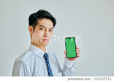 Young man in his 20s holding a smartphone Green background 123727721