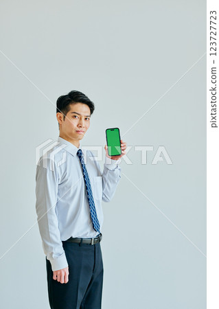 Young man in his 20s holding a smartphone Green background 123727723