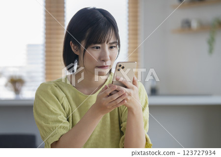 A woman in her 30s staring at her smartphone with a troubled look A woman in her 30s staring at her smartphone with a troubled look 123727934