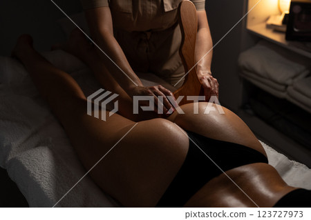Anti-cellulite massage on the stomach using wooden objects. Massage salon in a dark room. 123727973