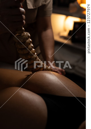 Anti-cellulite massage on the stomach using wooden objects. Massage salon in a dark room. 123727974