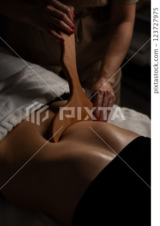 Anti-cellulite massage on the stomach using wooden objects. Massage salon in a dark room. 123727975