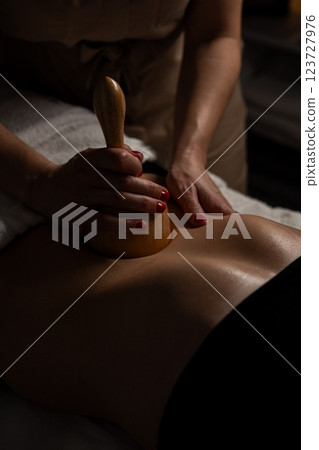 Anti-cellulite massage on the stomach using wooden objects. Massage salon in a dark room. 123727976