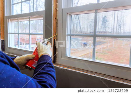 Contractor is sealing gaps around window frame with insulation foam during home renovation project 123728409