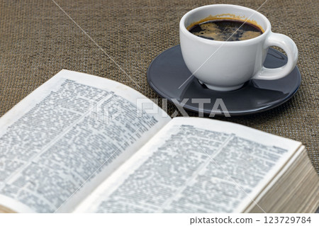 Coffee in a white cup on a black saucer with a book and morning essentials on the table. 123729784