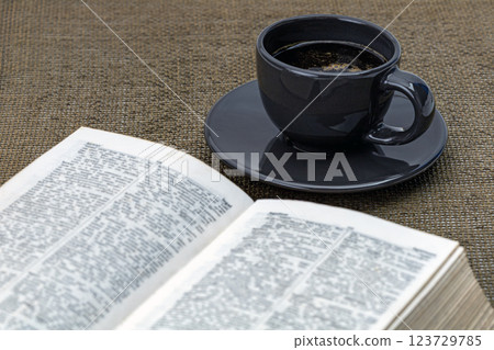 Coffee in a black cup  on a black saucer with a book and morning essentials on the table. 123729785