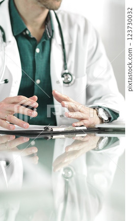 Male doctor using a clipboard and taking notes on glass desk in a medical office, close-up vertical view. Medicine concept Male doctor using a clipboard and taking notes on glass desk in a medical office, close-up vertical view. Medicine concept 123730032