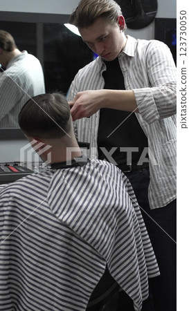 Professional barber grooming client's hair using electric clipper, delivering precise cut with skill in contemporary salon setting Professional barber grooming client's hair using electric clipper, delivering precise cut with skill in contemporary salon setting 123730050