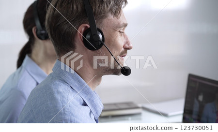 Focused male call center operator in blue casual shirt is assisting clients online, providing customer support and answering inquiries. Call center Focused male call center operator in blue casual shirt is assisting clients online, providing customer support and answering inquiries. Call center 123730051