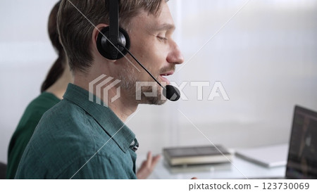 Focused male call center operator in green casual shirt is assisting clients online, providing customer support and answering inquiries. Call center concept 123730069