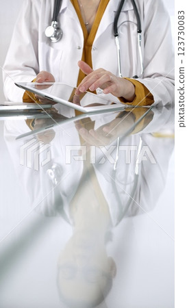 Unknown doctor woman wearing a stethoscope, yellow blouse under a lab coat, is using digital tablet in modern healthcare setting, interacting with patient data, vertical portrait. Medicine concept Unknown doctor woman wearing a stethoscope, yellow blouse under a lab coat, is using digital tablet in modern healthcare setting, interacting with patient data, vertical portrait. Medicine concept 123730083
