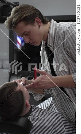 Professional barber trimming customer's hair with electric clipper, focusing on precise nape grooming within contemporary barbershop interior design Professional barber trimming customer's hair with electric clipper, focusing on precise nape grooming within contemporary barbershop interior design 123730121