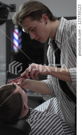 Professional barber trimming customer's hair with electric clipper, focusing on precise nape grooming within contemporary barbershop interior design Professional barber trimming customer's hair with electric clipper, focusing on precise nape grooming within contemporary barbershop interior design 123730123