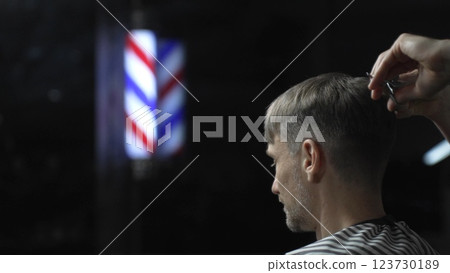 Professional barber grooming male client's hair with scissors, vintage barber pole framing traditional barbershop setting 123730189