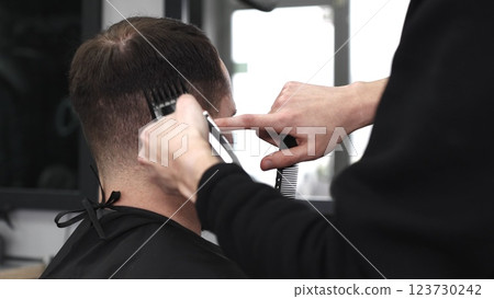 Skilled barber trimming client's hair using electric razor, creating contemporary hairstyle in modern barbershop setting with precise, professional technique 123730242