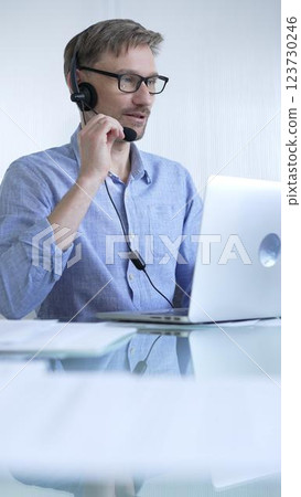 Male office worker demonstrates the significance of technology in modern business through client communication using laptop and headset. Business people concept Male office worker demonstrates the significance of technology in modern business through client communication using laptop and headset. Business people concept 123730246