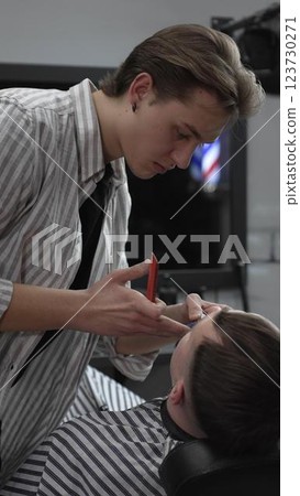 Professional barber trimming customer's hair with electric clipper, focusing on precise nape grooming within contemporary barbershop interior design Professional barber trimming customer's hair with electric clipper, focusing on precise nape grooming within contemporary barbershop interior design 123730271