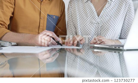 Two accountants are discussing a tax audit, using a laptop and reviewing documents at a glass table. Taxes, audit in business 123730277