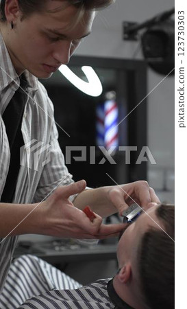 Professional barber trimming customer's hair with electric clipper, focusing on precise nape grooming within contemporary barbershop interior design Professional barber trimming customer's hair with electric clipper, focusing on precise nape grooming within contemporary barbershop interior design 123730303
