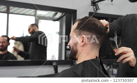 Skilled barber trimming client's hair using professional scissors, creating contemporary hairstyle in modern barbershop setting with precise, professional technique. Skilled barber trimming client's hair using professional scissors, creating contemporary hairstyle in modern barbershop setting with precise, professional technique. 123730307