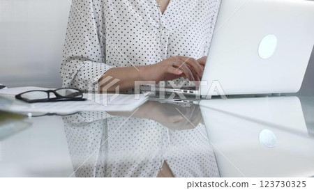 Businesswoman typing on laptop keyboard, preparing taxes and audit reports, with documents and eyeglasses on glass desk. Taxes, audit in business Businesswoman typing on laptop keyboard, preparing taxes and audit reports, with documents and eyeglasses on glass desk. Taxes, audit in business 123730325