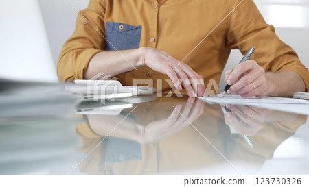 Businessman accountant wearing casual yellow shirt carefully reviewing financial reports using a calculator on office glass desk. Taxes, audit in business Businessman accountant wearing casual yellow shirt carefully reviewing financial reports using a calculator on office glass desk. Taxes, audit in business 123730326