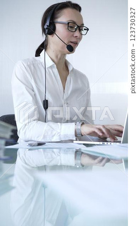 Female secretary wearing headset and working on laptop, providing customer support or online service. Business people concept Female secretary wearing headset and working on laptop, providing customer support or online service. Business people concept 123730327