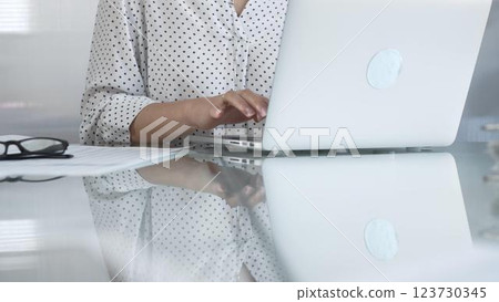Businesswoman typing on laptop keyboard, preparing taxes and audit reports, with documents and eyeglasses on glass desk. Taxes, audit in business Businesswoman typing on laptop keyboard, preparing taxes and audit reports, with documents and eyeglasses on glass desk. Taxes, audit in business 123730345