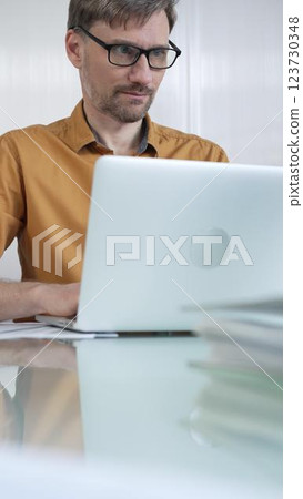 Focused businessman in yellow casual shirt is using laptop and thinking with hand on chin, working on a project in a modern office, vertical portrait. Business people concept Focused businessman in yellow casual shirt is using laptop and thinking with hand on chin, working on a project in a modern office, vertical portrait. Business people concept 123730348