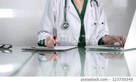 Woman doctor using a clipboard and taking notes on glass desk in a medical office, close-up view. Medicine concept 123730349