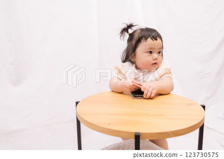 [Pigtailed baby standing on a table with smartphone] 123730575