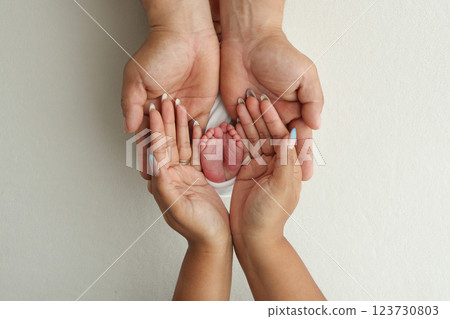 A father and mother hold the feet of a newborn child in a white blanket on a white background.. The feet of a newborn in the hands of parents. Photo of foot, heels and toes.The palms of the parents. 123730803