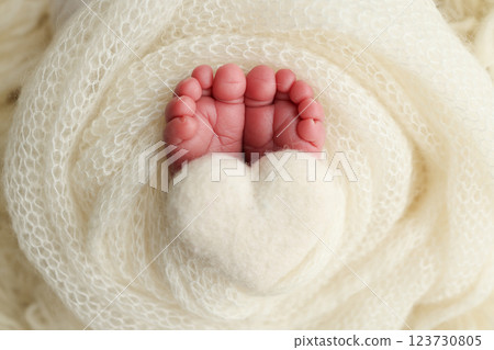 Soft feet of a new born in a white wool blanket. Close up of toes, heels and feet of a newborn. Knitted white heart in the legs of a baby. Macro photography.The tiny foot of a newborn baby 123730805