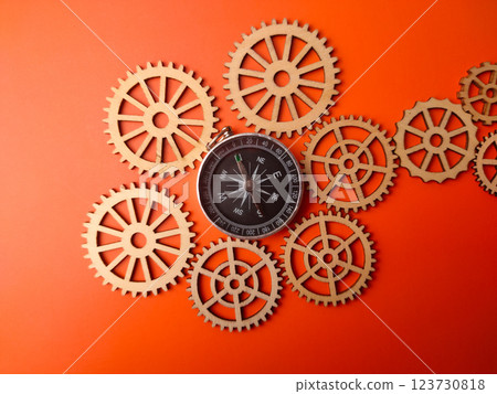 Closeup compass with wooden gear on a orange background. Closeup compass with wooden gear on a orange background. 123730818