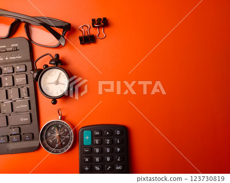 Top virw keyboard,clock,calculator,compass and glasses on a orange background with copy space.Business concept. 123730819