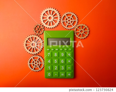Top view green calculator with wooden gear on a orange background. Business concept. Top view green calculator with wooden gear on a orange background. Business concept. 123730824