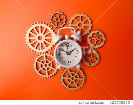Top view white alarm clock with wooden gear on a orange background. Top view white alarm clock with wooden gear on a orange background. 123730830