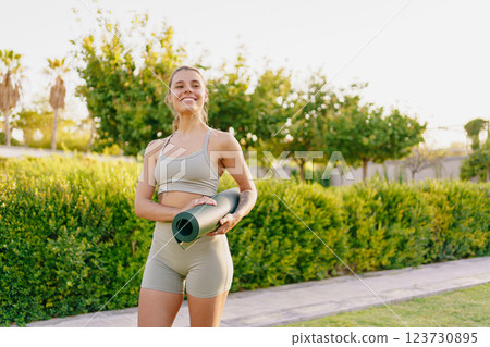 A Cheerful Young Woman Practicing Yoga with a Yoga Mat in a Beautiful Outdoor Setting A Cheerful Young Woman Practicing Yoga with a Yoga Mat in a Beautiful Outdoor Setting 123730895