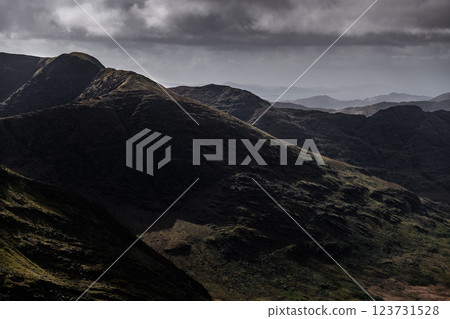 The photo depicts a series of mountain ranges. The closest range shows rocky, dark brown and black slopes. The photo depicts a series of mountain ranges. The closest range shows rocky, dark brown and black slopes. 123731528
