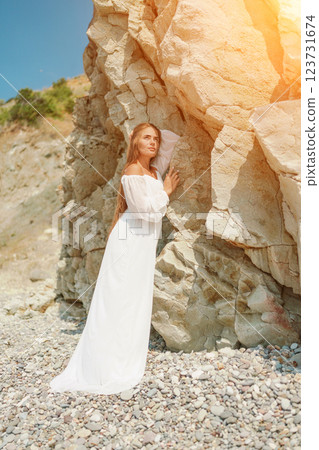 A woman in a white dress is standing on a rocky beach. Concept of serenity and tranquility, as the woman is enjoying the natural beauty of the beach. A woman in a white dress is standing on a rocky beach. Concept of serenity and tranquility, as the woman is enjoying the natural beauty of the beach. 123731674