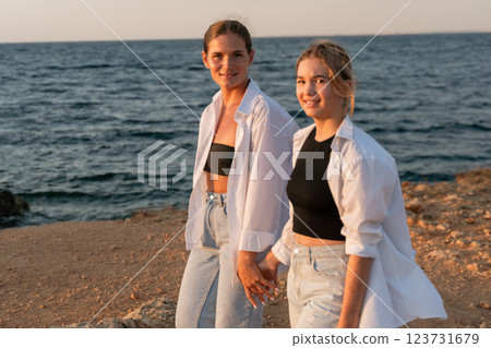 Women Beach Sunset Couple Holding Hands - Two women walk hand-in-hand on a beach at sunset. 123731679