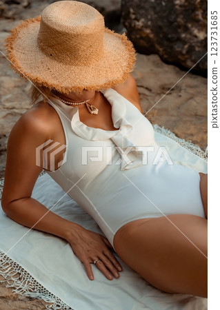 Woman, Beach, Swimsuit - Woman wearing a white swimsuit and a straw hat laying on a beach towel. 123731685